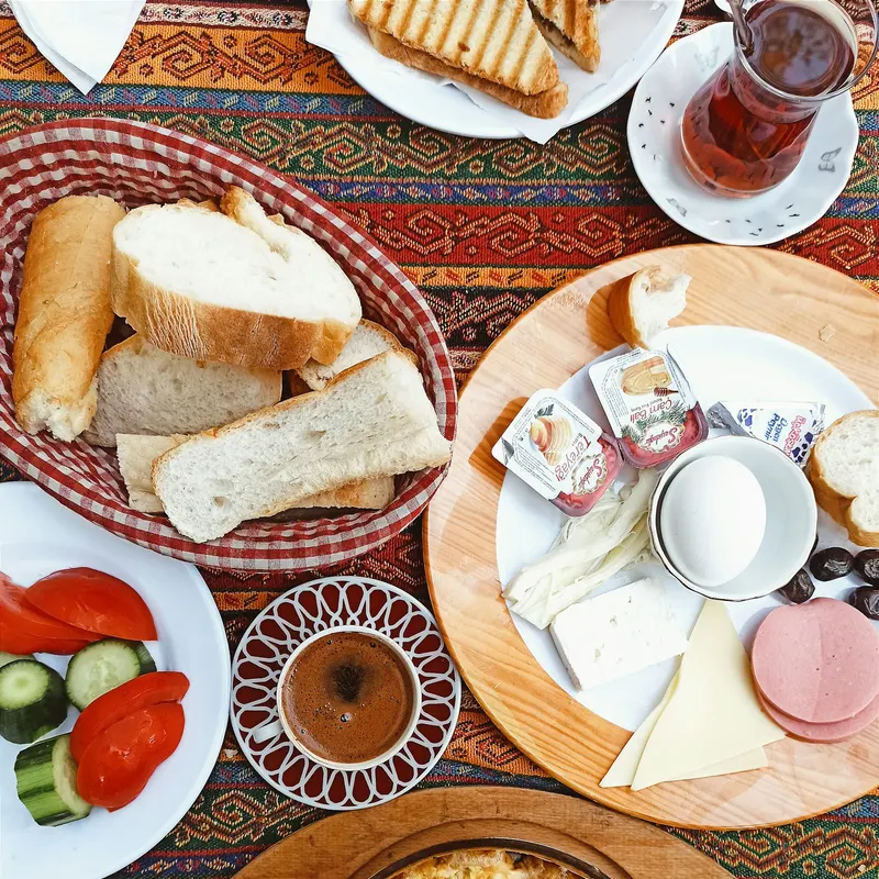 Kilim örtülü masada kahvaltı tabağı, tost, çay ve Türk kahvesi